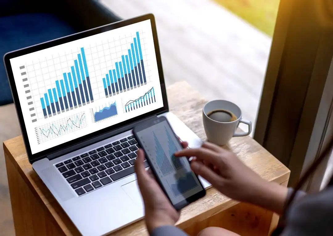 Hånd som trykker på en mobil med pc i bakgrunnen